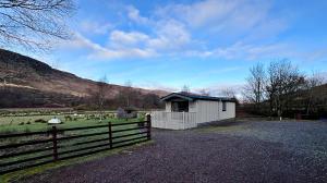 a building with a fence next to a field with sheep at Lapwing chalet in Crianlarich