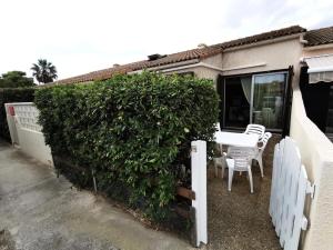 a patio with a white table and chairs next to a hedge at Résidence LES MAISONS DU PORT - Maisons & Villas pour 6 Personnes 74 in Port Leucate