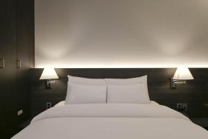 a large bed with white sheets and two lights on it at H Avenue Hotel Sangmu Branch in Gwangju