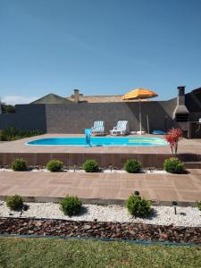 a swimming pool with two chairs and an umbrella at Casa ,piscina há 100 metros do mar ,24 pessoas in Capão da Canoa