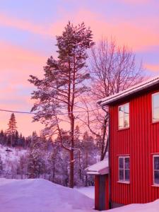 una casa rossa nella neve al tramonto di Skogsro Forest Hostel a Steinsholt