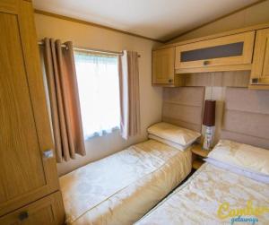 two beds in a small room with a window at MP639 - Camber Sands Holiday Park - 3 Bedroom - Sleeps 8 - Large gated decking - Close to facilities in Camber