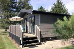 a tiny house with a deck and an umbrella at Tore Petty - Romantic lodge - spa bath and sauna in Brookland