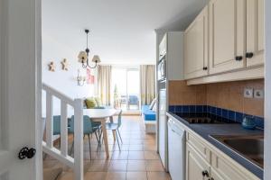 une cuisine avec des placards blancs et une table avec des chaises bleues dans l'établissement Les Appartements aux Restanques du Golfe de St Tropez - maeva Home - Appartem 04, à Grimaud