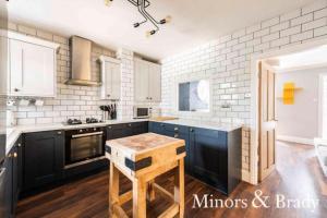 a kitchen with black cabinets and white brick walls at Modern terrace with large garden & standalone bar in Norwich