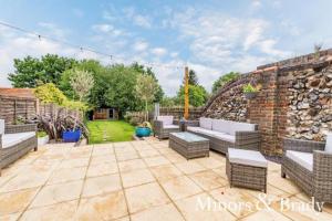 un patio con sofás y una pared de ladrillo en Modern terrace with large garden & standalone bar en Norwich