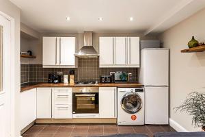 a kitchen with white cabinets and a washer and dryer at Cosy Garden Flat in Prestigious Residential Area in London