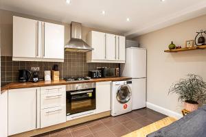 a kitchen with white cabinets and a washer and dryer at Cosy Garden Flat in Prestigious Residential Area in London