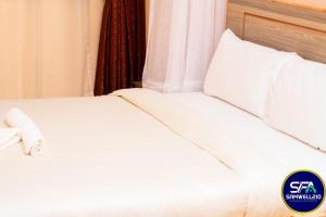 uma cama com lençóis brancos e almofadas num quarto em Samwell210 Furnished Apartments Kisumu em Kisumu