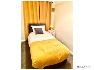 a bedroom with a bed with a yellow blanket at Spacious 3-Bed House with free parking in Hornchurch