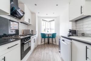 a white kitchen with a table and two green chairs at Stylish 3-bed near Camden Town & King's Cross in London