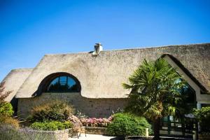 un bâtiment au toit de chaume avec un palmier dans l'établissement Résidence Le Saint Denac - maeva Home - Appartement 2 pièces 4 personnes - Prestige MAE-4234, à Saint-André-des-Eaux