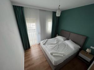a bedroom with a bed with white sheets and green walls at Wave Beachfront Apartments in Durrës