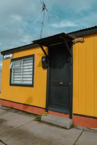 a yellow building with a black door and a window at Magic Hause Patagonia in Puerto Natales