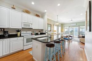 a kitchen with white cabinets and a kitchen island with bar stools at 93 Waters Edge - Townhome - Pool in Folly Beach