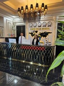 due persone in piedi dietro un bancone in un hotel di East Star Hotel a Samarkand