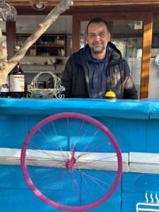 a man standing behind a blue counter with a red wheel at Eski Datça Pansiyon in Datca