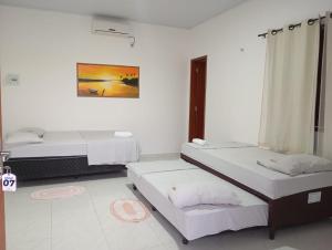um quarto branco com duas camas e um quadro na parede em Chalés Passagem do Canto em Barreirinhas
