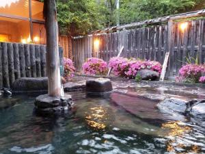 un laghetto in un cortile con fiori e recinto di Oshuku Onsen Hotel Uguisu - Vacation STAY 27315v a Shizukuishi