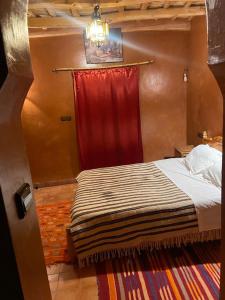 een slaapkamer met een bed met een rood gordijn bij Gîte d'étape Tamaloute in Bou Drarar