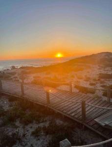 puesta de sol sobre una playa con un paseo marítimo de madera en Amar a Costa, en Costa de Lavos