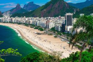 Blick auf einen Strand mit Gebäuden und Palmen in der Unterkunft Vista Mar - Studio em Copacabana a 1 min da praia e próximo ao metrô in Rio de Janeiro