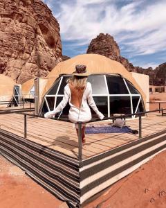 a woman is standing on a wooden deck in front of a van at RUM HiLTON lUXURY CAMP in Wadi Rum