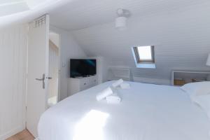 ein weißes Schlafzimmer mit einem weißen Bett und einem TV in der Unterkunft KER HIR - Charmante maison bretonne tout confort in Landunvez
