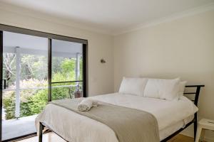 a white bedroom with a bed with a window at Narrawallee Beach House in Narrawallee