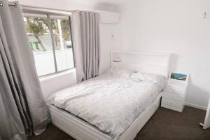 a white bedroom with a bed and a window at Fully renovated 3 bedroom house & Free Parking in Gold Coast