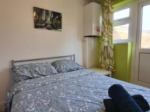 ein Schlafzimmer mit einem Bett mit blauer Decke und einem Fenster in der Unterkunft London Ilford Rooms in Goodmayes