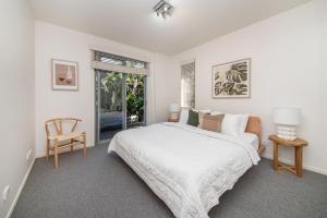a white bedroom with a bed and a chair at Heart of Hampton by the Beach in Melbourne