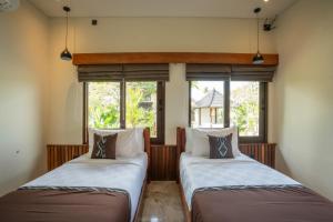 two beds in a room with two windows at Oma Ubud in Ubud