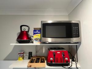a microwave oven sitting on a shelf with a red toaster at Country charm coastal living in Tura Beach