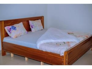 una cama de madera con sábanas blancas y almohadas. en Planete Hotel, en Rubavu