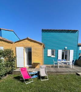 2 Gartenstühle, ein Tisch und ein blaues Haus in der Unterkunft Maison en résidence avec piscine in Le Château-dʼOléron