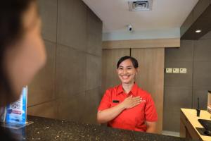 a woman in a red shirt standing in front of a mirror at Metland Hotel Cirebon by Horison in Cirebon