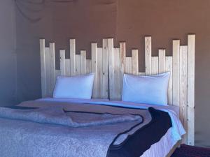 a bed with a wooden headboard with white pillows at Sahara wellness camp in Merzouga