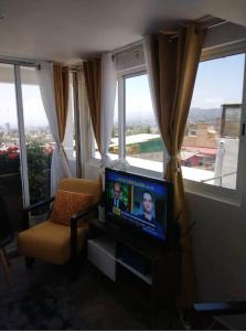 ein Wohnzimmer mit einem TV, einem Stuhl und Fenstern in der Unterkunft ¡Intimo, pequeño, confortable, mejor que hotel! in Mexiko-Stadt