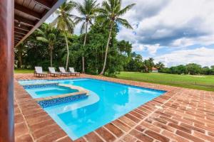 a pool with chairs and palm trees in a backyard at Beautiful and Comfortable Four Bedroom Villa in Cajuiles