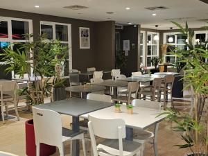 un ristorante con tavoli, sedie e piante di Campanile Hotel Chantilly a Chantilly