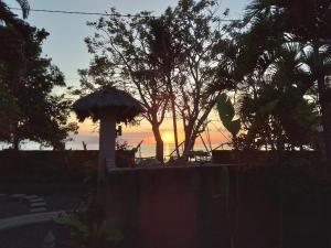 a sunset over the ocean with an umbrella and trees at Villa del Mar Amed Bali in Amed