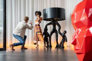 een man die een foto neemt van een vrouw die naast een standbeeld staat bij art'otel amsterdam, Powered by Radisson Hotels in Amsterdam