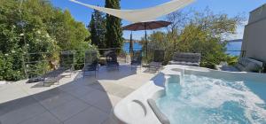 a hot tub with chairs and an umbrella on a patio at Jacuzzi, summer kitchen, gardens, 20m to beach - Villa Casa Plaza in Seget Vranjica