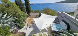 a white umbrella on the side of a house with the water at Jacuzzi, summer kitchen, gardens, 20m to beach - Villa Casa Plaza in Seget Vranjica