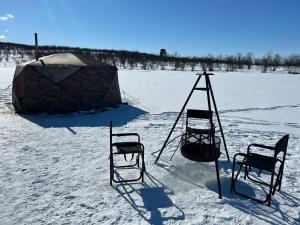 two chairs and a yurt in a snow covered field at Aurora Tent Camp in Karasjok