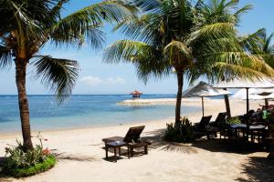 uma praia com cadeiras e palmeiras e o oceano em Four Star by Trans Hotel em Sanur