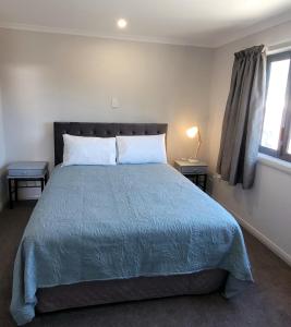 1 dormitorio con 1 cama con edredón azul y ventana en The Old Parsonage en Reefton