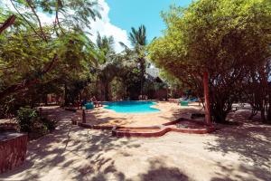 a swimming pool with trees and people sitting around it at Demani Lodge Zanzibar in Paje