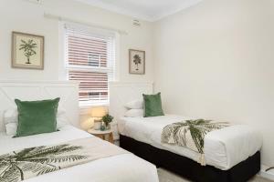 Spacious 2-Bed Apartment in the heart of Manly في سيدني: سريرين في غرفة بيضاء مع وسائد خضراء